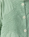 Close-up of textured pintuck and smocking-inspired stitching onPowder Green Jacket.