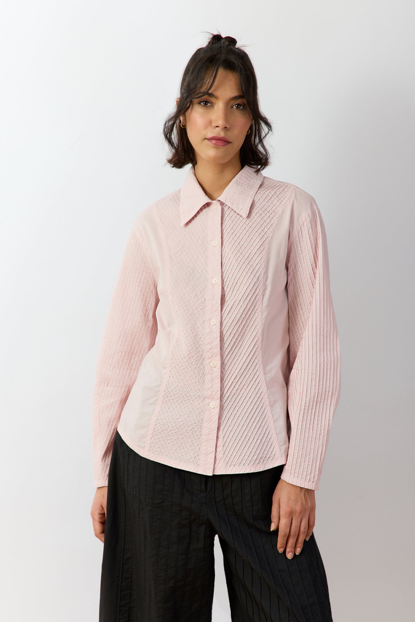 Woman wearing a light pink textured shirt and black pants on a white background