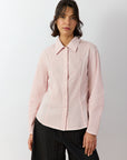 Woman wearing a light pink textured shirt and black pants on a white background