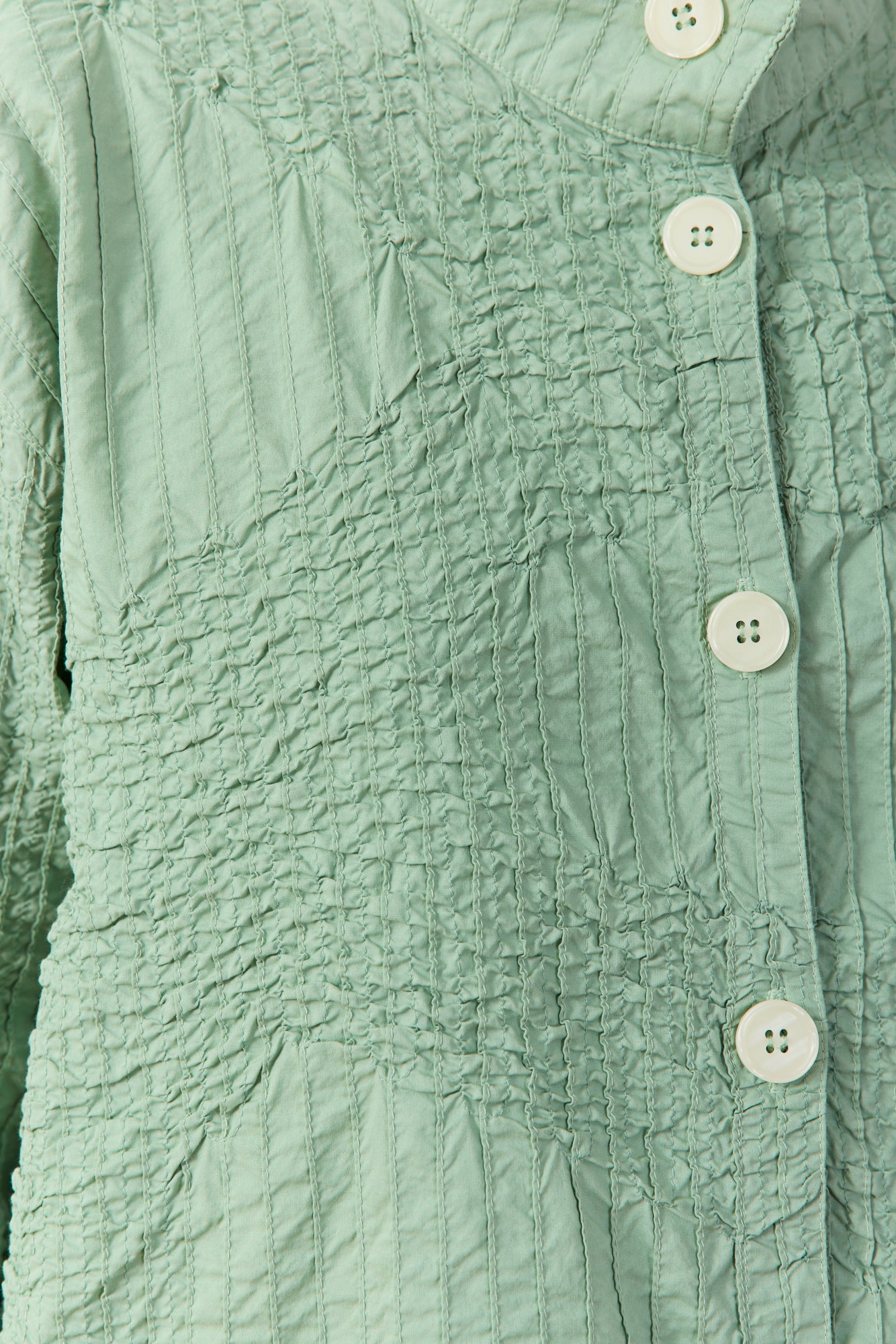 Close-up of textured pintuck and smocking-inspired stitching onPowder Green Jacket.