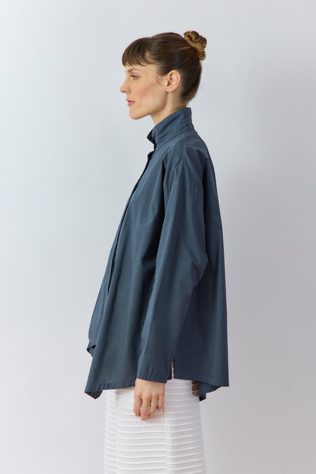 Side profile of the Ashin Shirt in Stone Blue highlighting the architectural asymmetric hem.